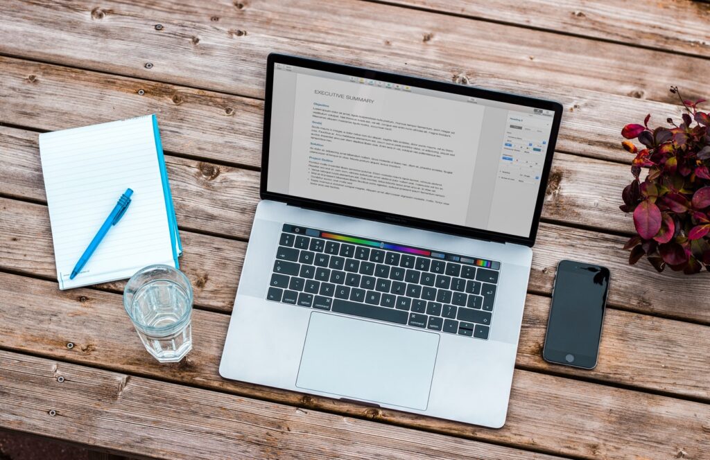 silver MacBook beside space gray iPhone 6 and clear drinking glass on brown wooden top photo
