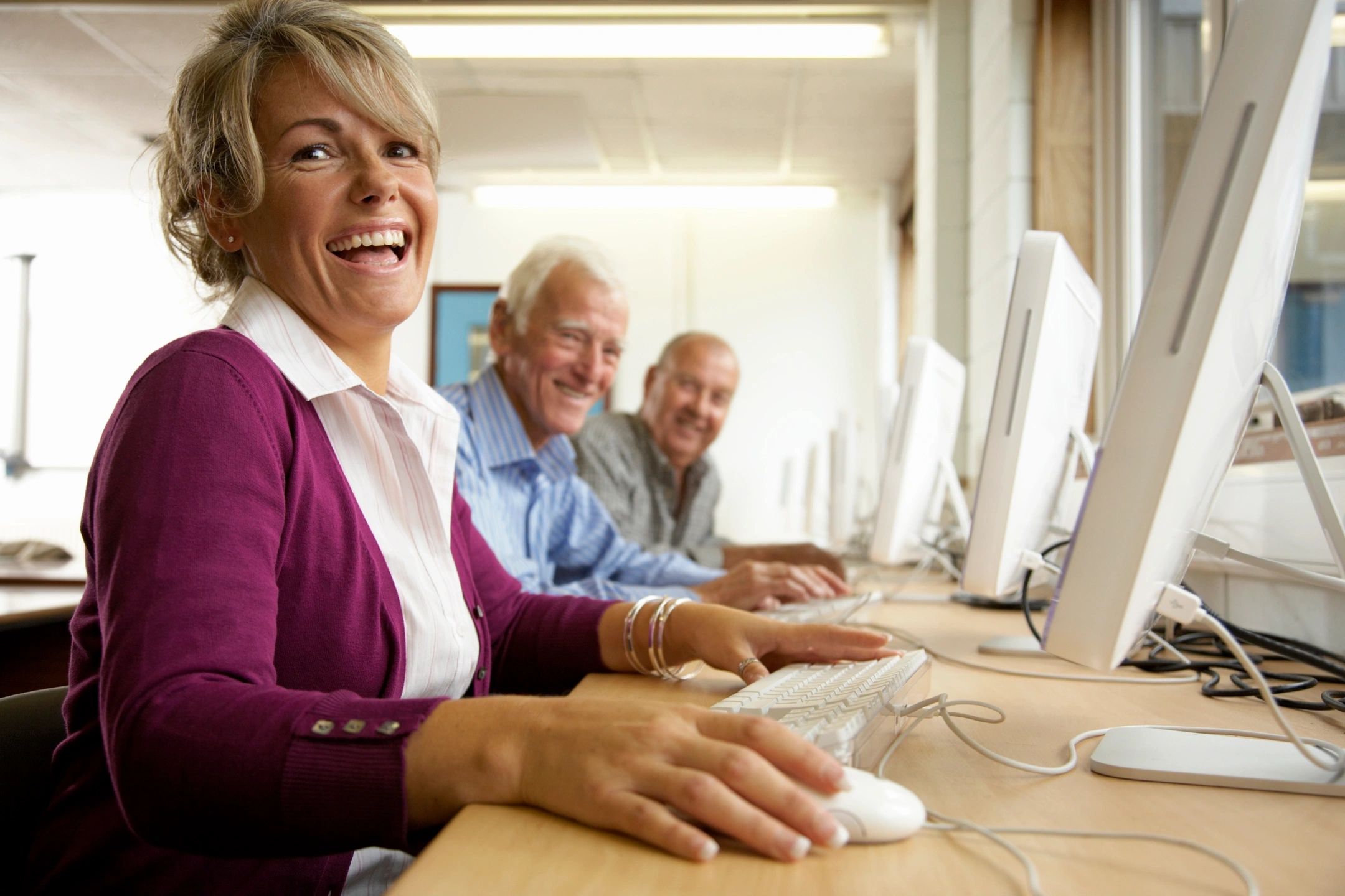 Two older men and one older woman sit at computers, smiling.