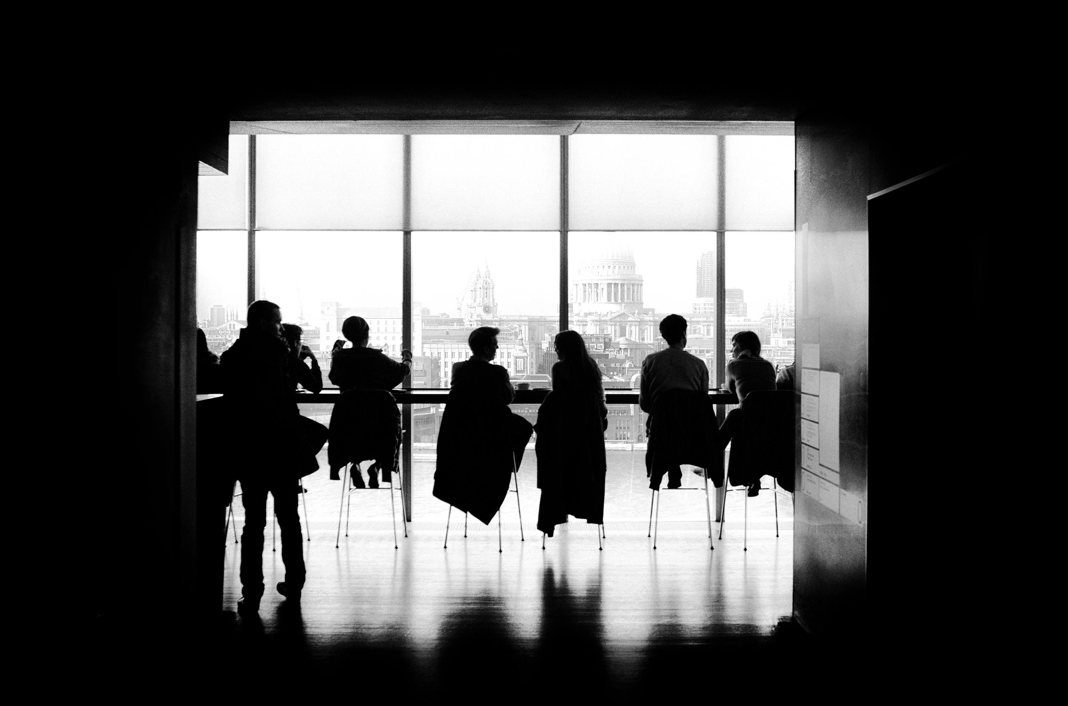 People sitting in chairs side by side in silhouette against a window.